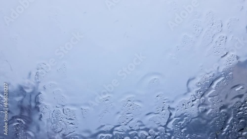 Rain hitting car window on blurred nature background.