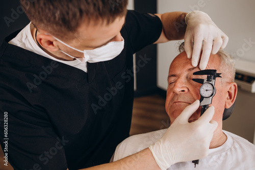 a plastic surgeon measures old senior man's eyelid with a ruler photo