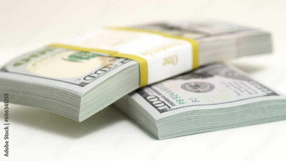 stack of bank bundles with US dollars on a white background. Close-up shot of new, freshly printed hundred-dollar bills rotating on a table. cash flow, business investment, or big money concepts. stack of bank bundles with US dollars on a white background. Close-up shot of new, freshly printed hundred-dollar bills rotating on a table. cash flow, business investment, or big money concepts.