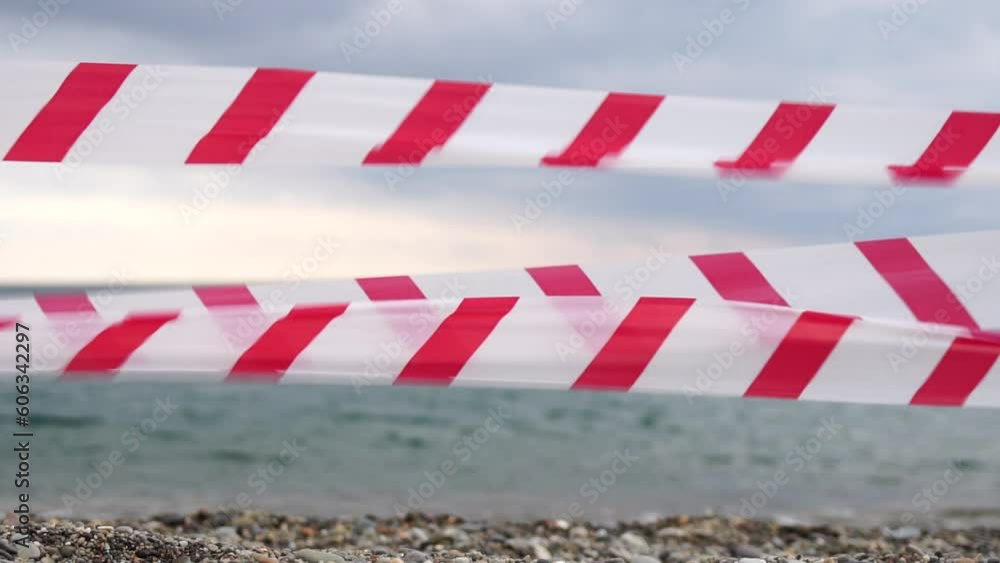 Red white warning tape barrier ribbon swinging in the wind across exotic sea beach background without people. No entry Red White caution tape. No holiday concept, delayed travel, no summer plans Red white warning tape barrier ribbon swinging in the wind across exotic sea beach background without people. No entry Red White caution tape. No holiday concept, delayed travel, no summer plans