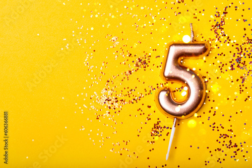 Gold candle in the form of number five on yellow background with confetti.