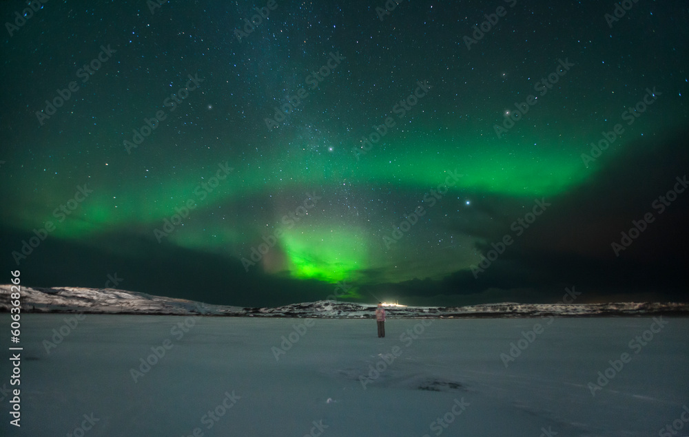 night landscape with northern lights and aurora by the sea in winter with a man in the frame