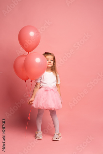 little girl in a white t-shirt and a pink tutu with balloons on pink background