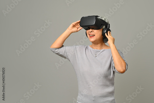 Elderly woman experiencing technology and innovation via VR headset isolated on gray background