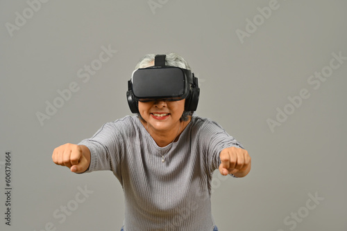 Cheerful senior woman with virtual reality glasses simulating of driving car in VR glasses isolated on white background