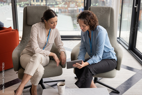 Female business executives meeting in office atrium reception looking at a digital tablet photo