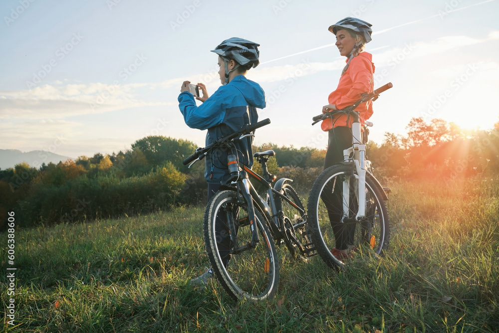 Mother and son ride bike outdoors. Happy cute boy in helmet to riding a bike in park on green meadow at sunset time. Family weekend. mothers Day