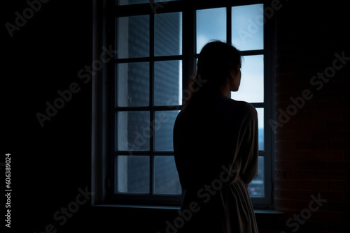 rear view of Lonely woman standing in the dark behind the window looking © alisaaa