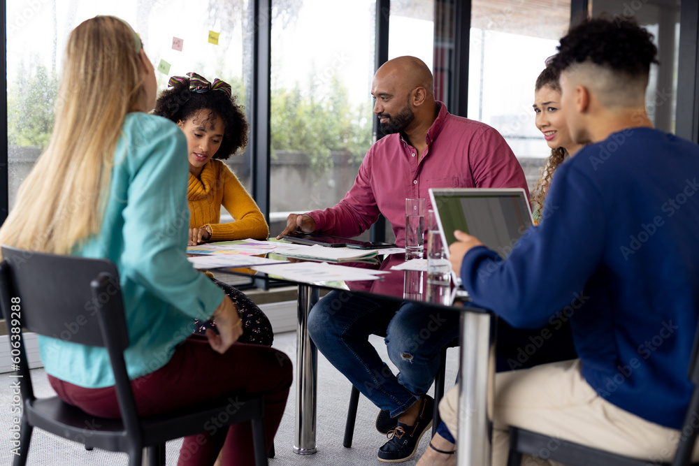 Busy diverse fashion designers using laptop and discussing work at meeting in office, unaltered Busy diverse fashion designers using laptop and discussing work at meeting in office, unaltered