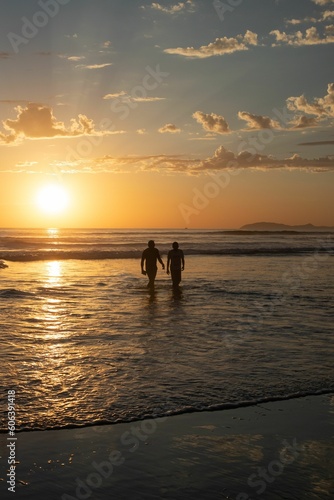 Silhouette view of two people walking out of the water at sunset