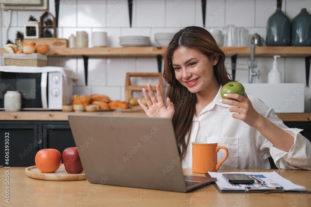 smiling young woman on a video call with colleagues, sitting on a kitchen with laptop computer, waving smiling young woman on a video call with colleagues, sitting on a kitchen with laptop computer, waving