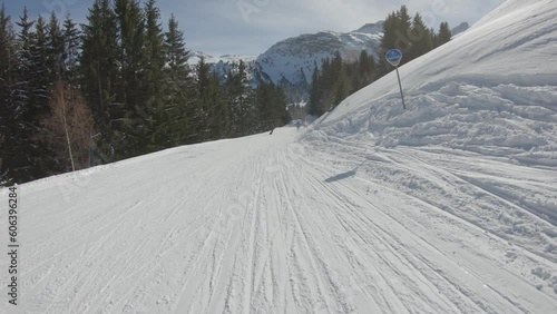 Going down a ski slope between the trees on a sunny day with skiers and snowboarders far away