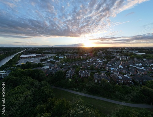 Aerial view of houses surrounded by green trees with a cloudy sunset sky in the background