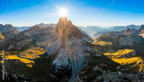 Mountain landscape of Three Peaks of Lavaredo at sunrise. Sunny jagged peaks and broad hilly shaded highlands covered with grass and sand aerial view