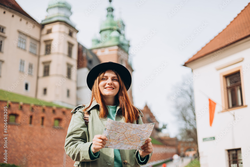 Happy optimistic woman smiling confident holding city map at street. Attractive young female tourist in hat is exploring new city. Traveling Europe in spring. Urban lifestyle banner