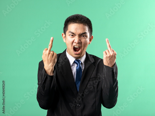 Fotografía A portrait of an Asian man wearing a white shirt and a black suit, showing both of his middle fingers, isolated on a green background