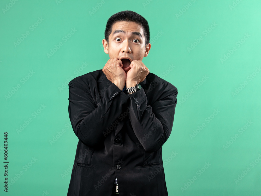 A portrait of an Asian man wearing a white shirt and a black suit, looking scared, and touching his chin with his hand, isolated on a green background. A portrait of an Asian man wearing a white shirt and a black suit, looking scared, and touching his chin with his hand, isolated on a green background.
