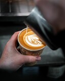 Vertical shot of a man making a drawing on a cappuccino in his hand with milk