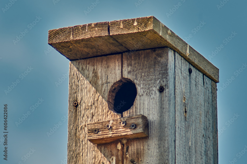 An old wooden birdhouse with a hole and a landing bar against the sky