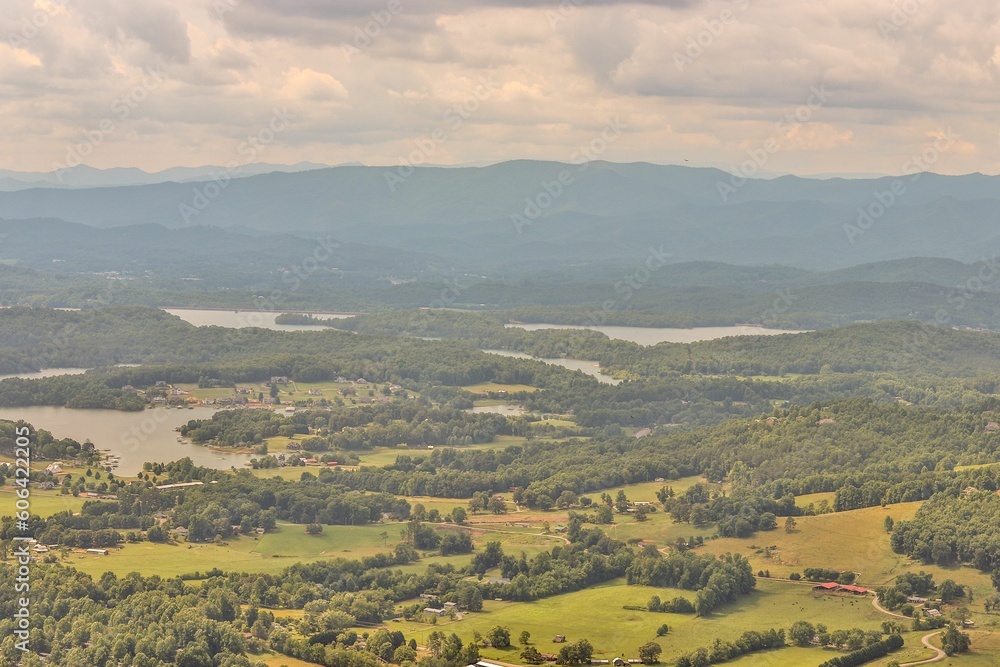 Aerial view of vast green fields with thick trees, mountains and lakes under a cloudy sky at sunset