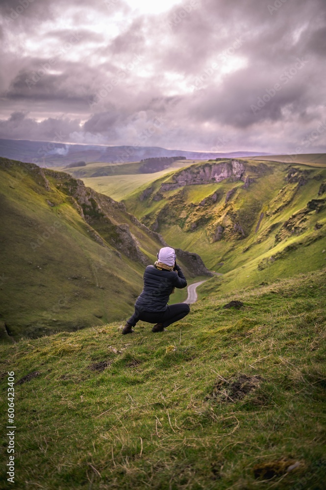 Vertical of a photographer capturing a natural scenery while squatting on a mountain slope