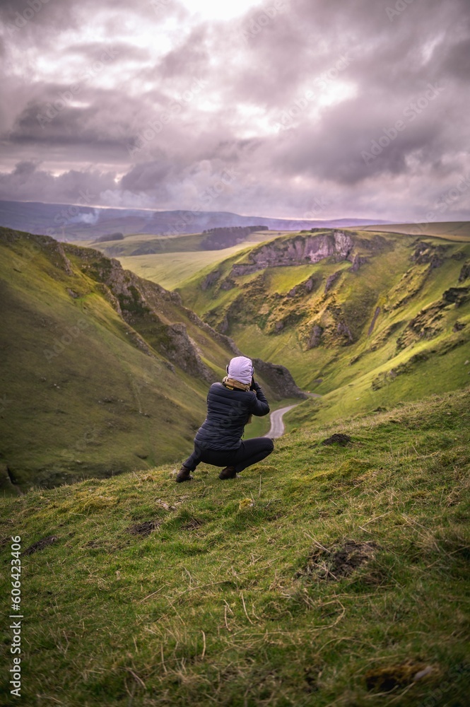 Vertical of a photographer capturing a natural scenery while squatting on a mountain slope Vertical of a photographer capturing a natural scenery while squatting on a mountain slope