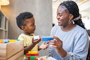 A cute little African child plays with colorful didactic educational toys. His proud mother supports him. Kindergarten teacher with child.