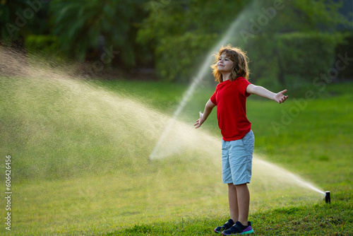 Kids play with water hose, sprinkler watering grass in the garden. Summer garden outdoor fun for children. Boy splashing water on hot summer day. Kid watering plants and grass in backyard.