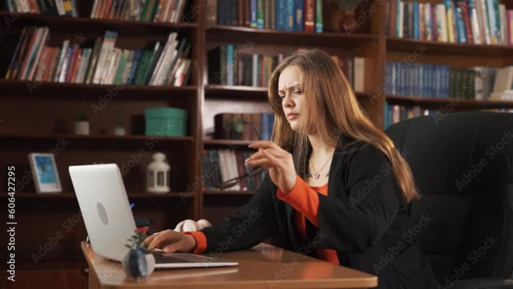 The girl is sitting at the table and working on a laptop. She rests her head on her hand, typing something. She looks very tired, and eventually, she props her head up and falls asleep. The girl is sitting at the table and working on a laptop. She rests her head on her hand, typing something. She looks very tired, and eventually, she props her head up and falls asleep.