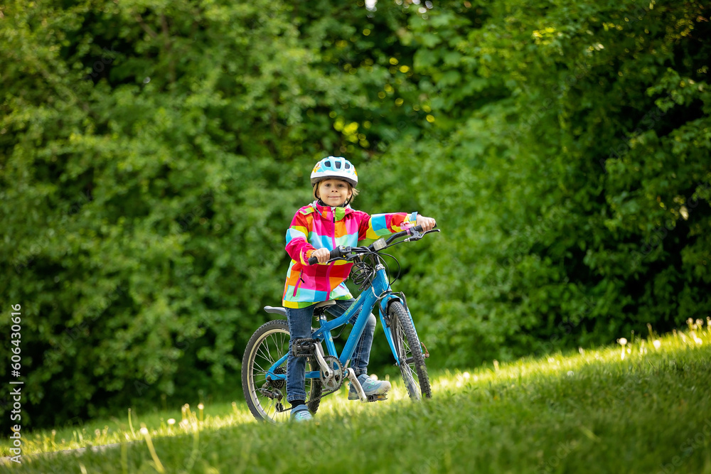 Happy kid boy, having fun in park with a bicycle on beautiful day. Active child wearing bike helmet