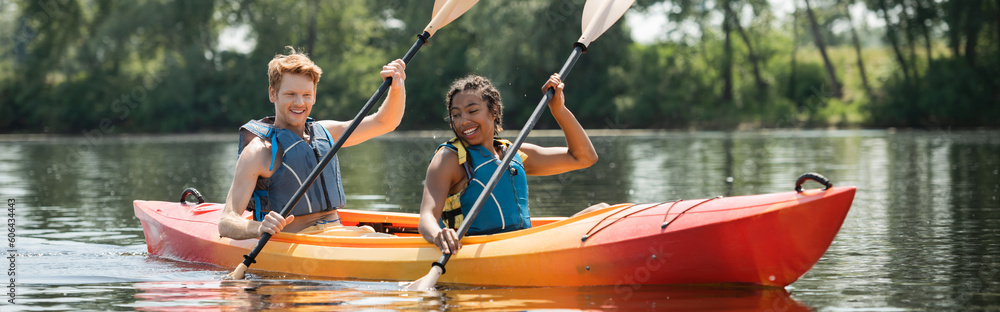Εκτύπωση καμβά smiling and active multiethnic friends in life vests paddling in sportive kayak