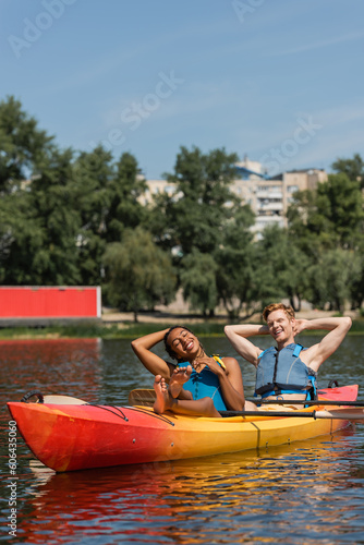pleased and barefoot african american woman and smiling redhead man in life vests relaxing with closed eyes in sportive kayak during summer weekend on lake © LIGHTFIELD STUDIOS