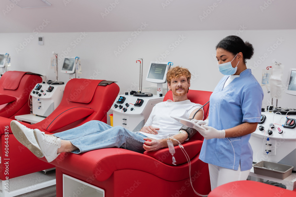 Φωτογραφία multiracial nurse in medical mask and latex gloves using digital tablet near red
