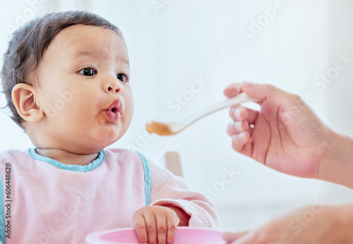 Mother, feeding baby girl and spoon in home, kitchen or living room for nutrition, growth or health. Woman, hand and food for infant child for help, eating or balance in diet for development in house
