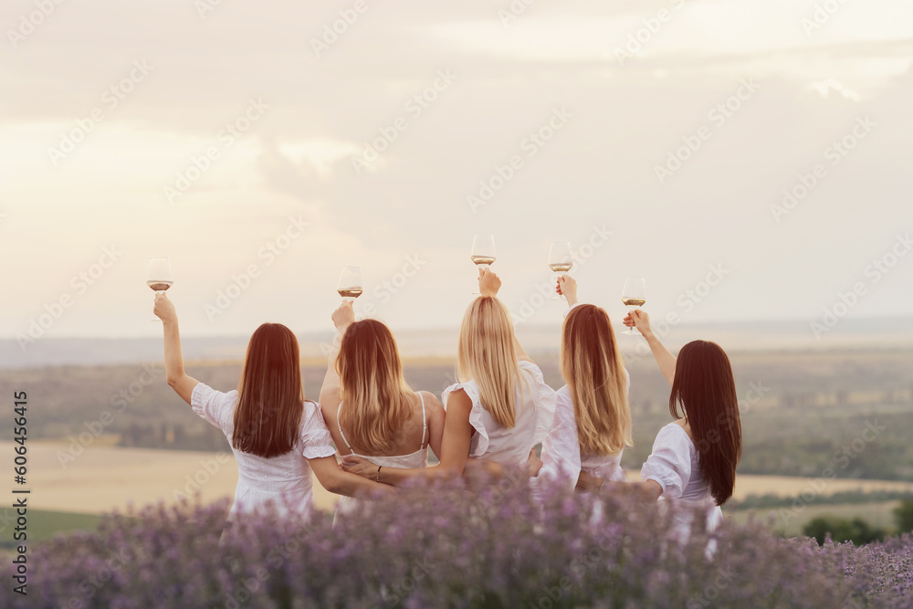 Young women in a white dresses standing with hands up in the middle of a lavender field in the sunny summer day.