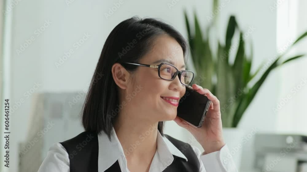 Chest up portrait of young Asian female manager making phone call and looking at camera working in insurance agency Chest up portrait of young Asian female manager making phone call and looking at camera working in insurance agency