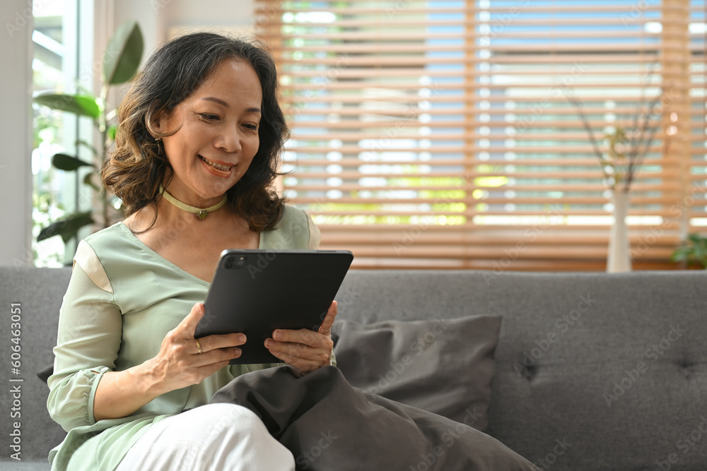 Domestic life concept with middle aged Asian woman looking happy using digital tablet while sitting on sofa. Domestic life concept with middle aged Asian woman looking happy using digital tablet while sitting on sofa.