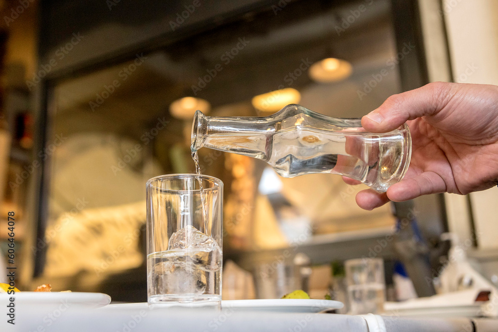 Greek tsipouro being poured into a glass with ice cubes at a taverna. Soft focus