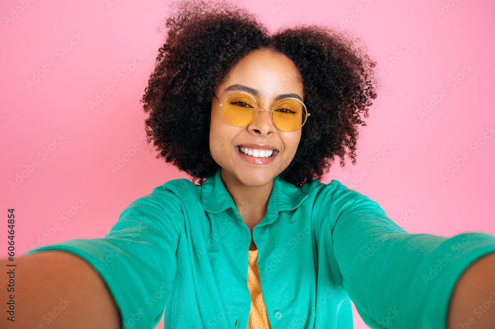 Lovely cheerful fashionable brazilian or hispanic woman, blogger, wearing green casual shirt and trendy glasses, taking selfie photo, looks at camera, smiles, stand on isolated pastel pink background Lovely cheerful fashionable brazilian or hispanic woman, blogger, wearing green casual shirt and trendy glasses, taking selfie photo, looks at camera, smiles, stand on isolated pastel pink background