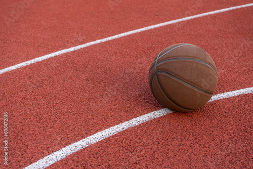 Basketball ball on the ground. Close-up ball on the red court. Basketball on the street or indoor court. Sports gear without people. Minimalism. Template, sport background 