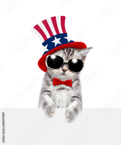 Cute kitten wearing like Uncle Sam looks above empty white banner. isolated on white background © Ermolaev Alexandr