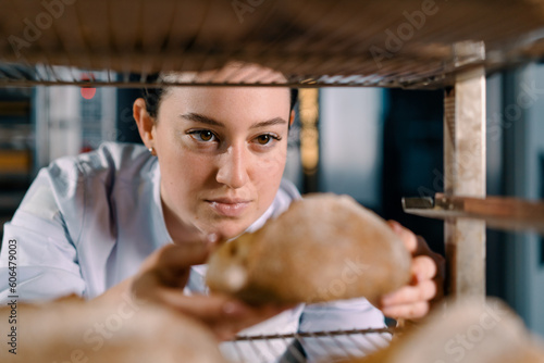 attractive female baker between shelves looking and checking freshly baked bread very carefully in bakery industry © Guys Who Shoot