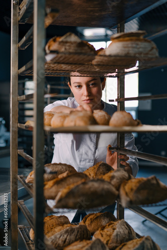 attractive female baker between shelves looking and checking freshly baked bread very carefully in bakery industry