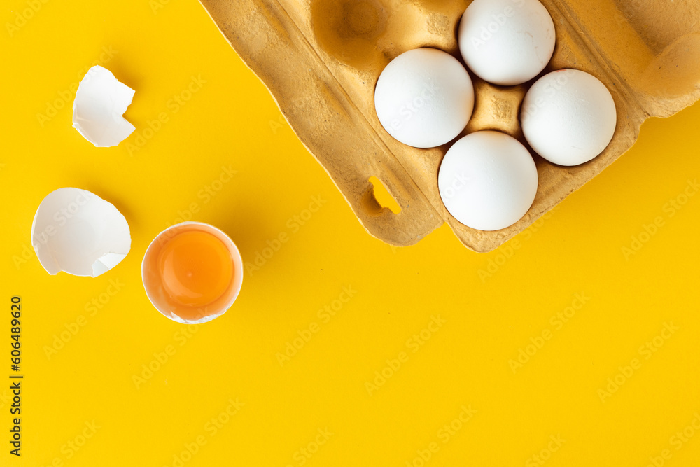 Flat lay of white eggs in the carton brown box on the yellow background. Top view of broken egg with white shell. Copy space for a free text.