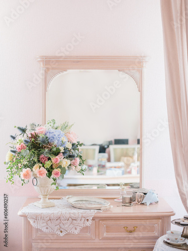 Fototapeta Naklejka Na Ścianę i Meble -  Women's pink dressing table in vintage style with a mirror. On the dressing table a bouquet of peonies, roses and hydrangeas, a metal tray, a box of pearls, perfume. Company faux french style.