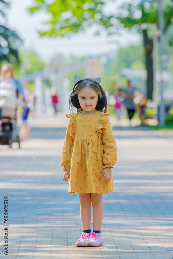 Fototapeta premium A little girl in a yellow dress stands on a street.