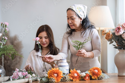 Portrait of a beautiful retired Asian woman focuses on arranging a vase with fresh flowers in a workshop. Lifestyle concept