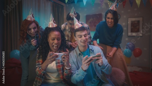 An African American girl and a Caucasian guy are playing an online game on their phones, their friends are supporting them by standing behind them. Competition in online games.