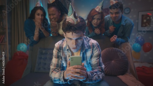 A guy is playing an online game on his phone, his friends are watching him tensely standing behind him. Games, entertainment at home parties.