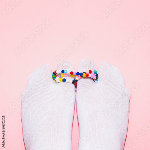 Two feet in white tabi socks are linked with colored bead necklaces on a pink  background. Creative concept,  top view, flat lay photo